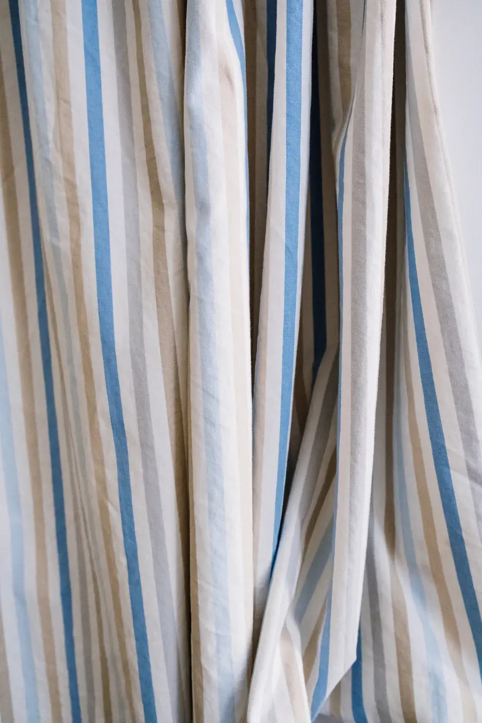 Woven curtain fabric with blue and neutral stripes in hanging folds